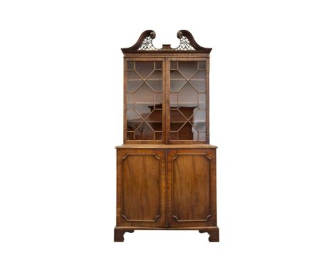 A George III mahogany cupboard bookcase with a carved and lattice worked swan neck pediment above a pair of astragal moulded 