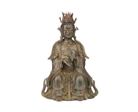 A Chinese bronze figure of Guanyin, seated wearing long robes and holding a mirror, traces of red pigment and gilding through