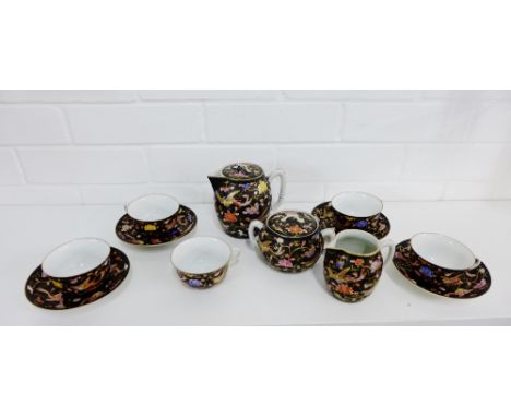 A Japanese porcelain tea set painted with flowers and foliage and coloured enamels to a black ground comprising six cups, fou