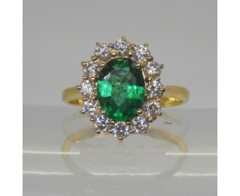 An 18ct gold emerald and diamond cluster ring, set with a 8.6mm x 6.4mm x 3.8mm, oval emerald, further set with a halo of bri