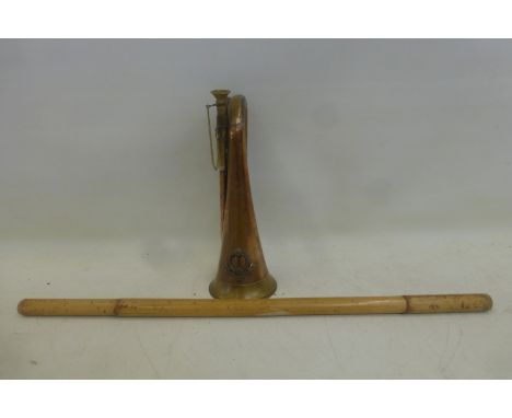 A copper and brass military bugle with applied badge and a bamboo swagger stick.