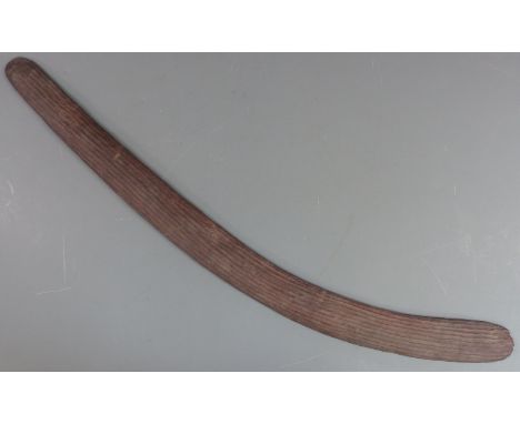 A 19thC Australian Aboriginal boomerang or throwing stick with carved parallel lines and adzed verso, length 71cm