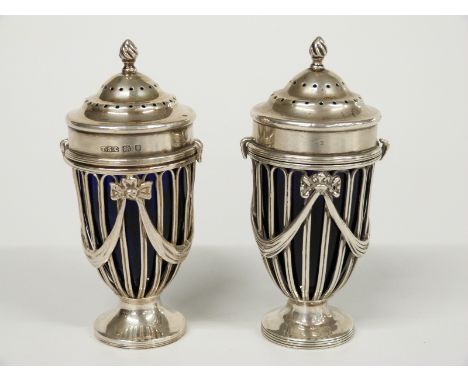 A pair of hallmarked silver pedestal peppers or casters with blue glass liners, swag decoration and bayonet locking lids, one
