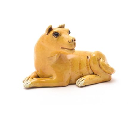 A Chinese export yellow-glazed model of a dog, Kangxi, recumbent with head turned to one side with brown glazed eyes and whit