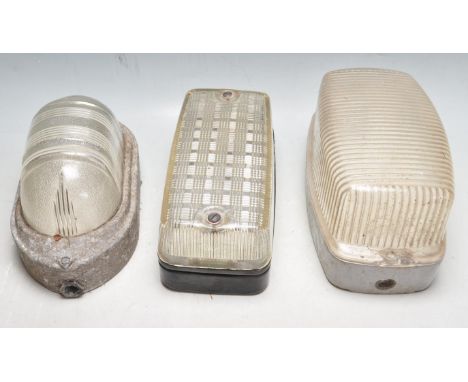 A collection of three retro vintage industrial exterior bulkhead lights having moulded plastic shades with cast metal frames.