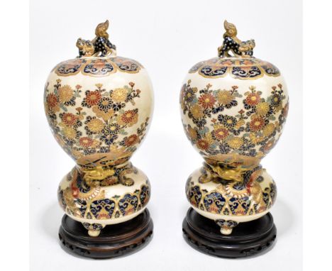 A pair of Japanese Satsuma incense burners, the circular covers with shishi dog surmounts above bulbous body painted with flo