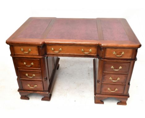 A reproduction pedestal desk with leatherette inset top, quarter turned columns and an arrangement of nine drawers, on ogee b