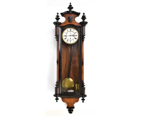 A walnut and stained beech Vienna-style wall clock with turned pendants, finials and female mask detail, the circular enamell