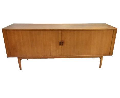 A mid-century teak sideboard with two roller shutter doors enclosing fitted drawers, raised on turned column supports, length