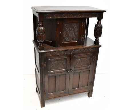 A reproduction oak court cupboard with single door to upper section, twin carved and panelled doors enclosing single shelf on
