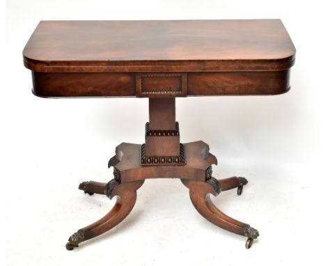 An early 19th century mahogany card table on quadripartite base to four outswept supports terminating in brass paw caps on ca