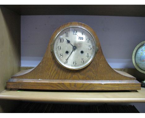 An Oak Veneered Mantel Clock, arched Napoleon hat case, silvered dial, black Arabic numerals on bun feet.