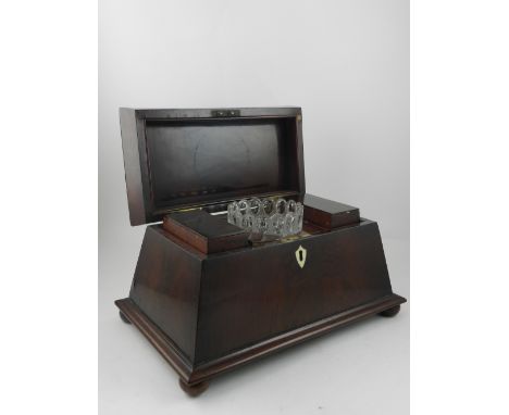 An early Victorian mahogany sarcophagus tea caddy, the hinged top enclosing two canisters and mixing bowls, raised on flatten