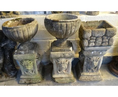 Pair of reconstituted stone garden urns with associated mask pillars together with another planter on similar pillar.  (3)  (