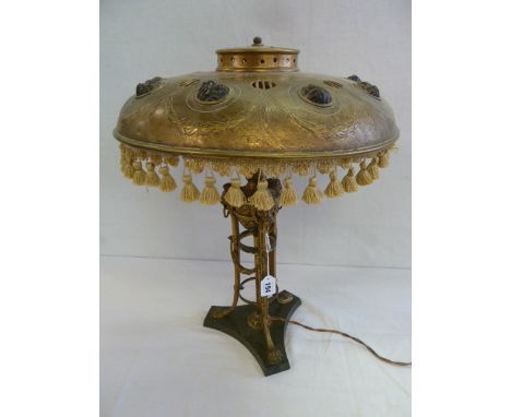 Early 20thC gilt metal triform base table lamp with lion mask drop handles and paw feet with 'jewelled' dome shade 