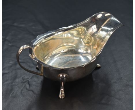 An Elizabeth II silver sauce boat, having a Chippendale style rim and generous spout opposed by a c-curve handle, raised on t