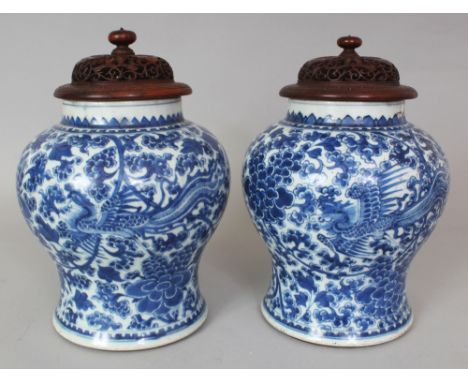 A GOOD PAIR OF CHINESE KANGXI PERIOD BLUE & WHITE PORCELAIN PHOENIX JARS, with good quality pierced and carved wood covers, 1