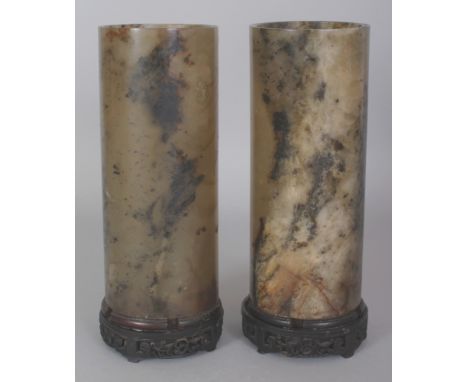 A PAIR OF EARLY 20TH CENTURY CHINESE JADE CYLINDRICAL VASES, each supported on a fixed carved wood stand, the predominantly d