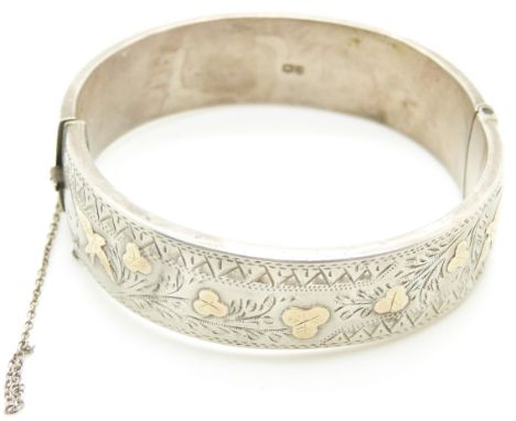 A silver bangle with engraved decoration and applied gold detail