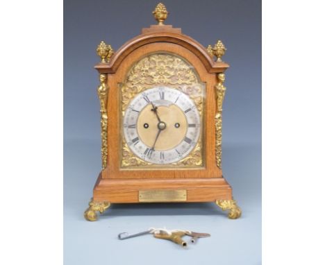 Goldsmiths Company of London Edwardian oak cased mantel clock with brass figural and floral decoration, the silvered Roman ch