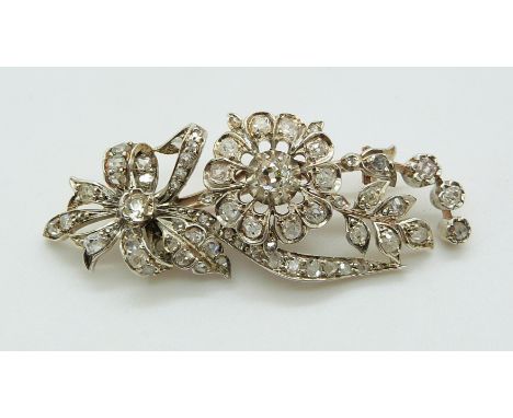 An early 20thC gold brooch set with diamonds in a floral, bow and foliate design, 6cm long