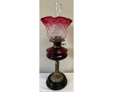 A 19thC brass and cranberry glass oil lamp on a black ceramic plinth. 64cm to top of chimney.Condition ReportGood condition.