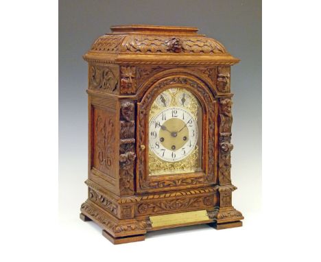 Early 20th Century heavily carved oak cased bracket clock having mask head and floral decoration, the arch shaped gilt dial w