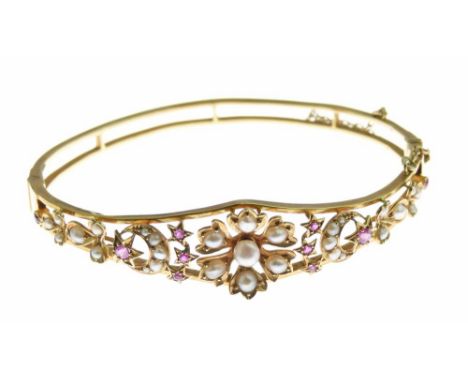Seed pearl and ruby hinged bangle tagged '18k', the frontispiece with flowerhead, star and crescent motifs in the late Victor