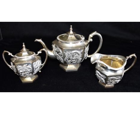 A CHINESE SILVER EXPORT THREE PIECE TEA SET  with raised dragon motif decoration, the hexagonal shaped small size tea set on 