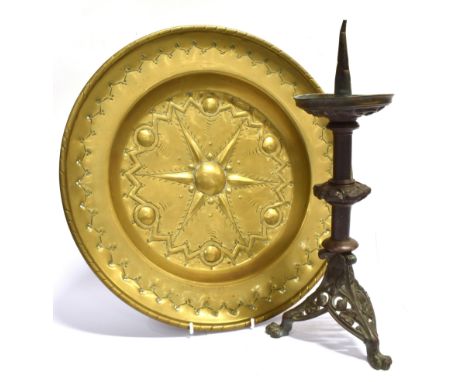 A BRASS ALMS DISH with embossed and chased decoration, 40.5cm diameter; and a pricket candlestick on triform base with claw f