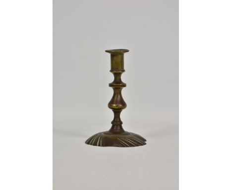 An early to mid 18th century brass candlestick, on a knopped and baluster stem, with a shallow, widely flared shaped square b
