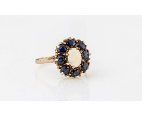 A 9ct yellow gold, opal and sapphire cluster ring, the 7 x 5mm. opal within a border of eight round cut sapphires, size P.. 