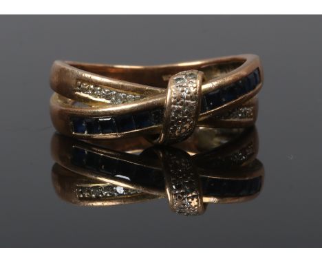 A 9ct gold crossover ring set with round cut diamonds and Princess cut sapphires, size P.