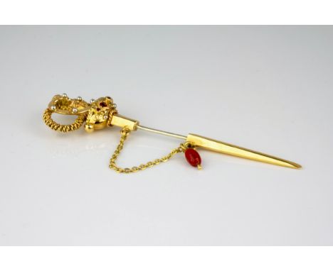 An 18ct gold stick pin in the form of a ceremonial sword, with steel pin, the guard set with red stones, 8.5cm. long.