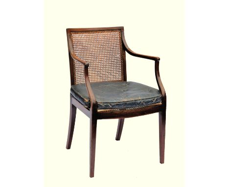 A George III mahogany elbow chair, the straight top rail over a caned back and seat, with leather buttoned squab cushion, wit