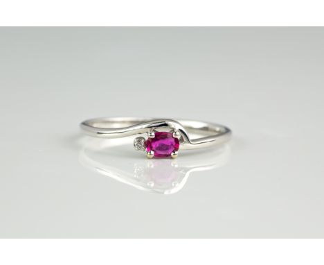 An 18ct white gold, ruby and diamond ring, the oval cut ruby beside a single brilliant cut diamond in a dainty cross over set