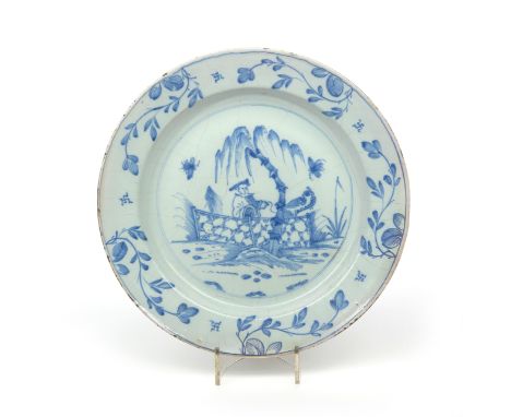 A large delftware charger  c.1760, painted in blue with a Chinese figure standing behind an ornamental fence on which perches