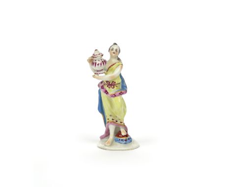 A miniature Bow figure of a Classical maiden c.1760, standing and holding a covered urn, wearing a yellow robe edged in pink 