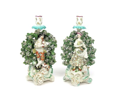 A pair of Derby candlestick figures of musical shepherds  c.1765, both standing before flowering bocage, he playing the flage