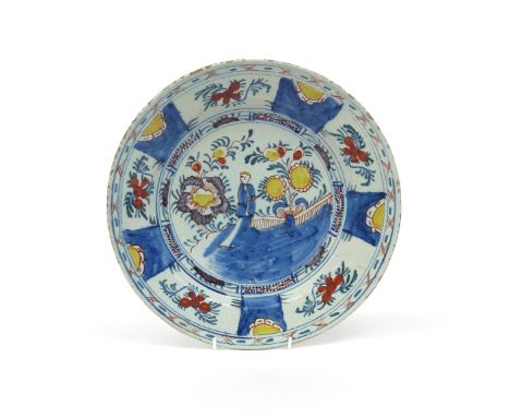 A delftware charger  c.1740, painted in polychrome enamels with a Chinese figure standing between large flowering plants, wit