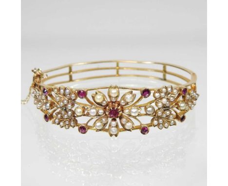 A gold, ruby and split pearl bangle, of hinged design, with safety chain, set with openwork floral designs, with seventy-four
