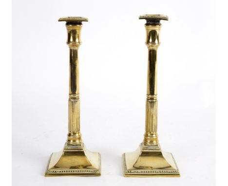 A pair of brass candlesticks, circa 1790, with square bead edged nozzles and with column sticks and square bases with bead ri