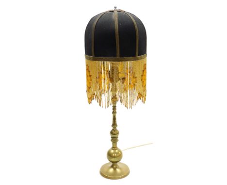 An early 20thC brass table lamp, the shade of black cylindrical form, with gilt trim and beaded hanging fringing, 58cm high o