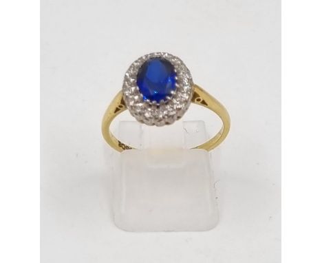 An 18K Yellow Gold Sapphire and Diamond Ring. Brilliant centre stone sapphire surrounded by bright white diamonds. Size O. 3.