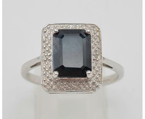 A 9 K white gold ring with an emerald cut dark blue sapphire and four diamonds on surrounding halo. Ring size: S, weight: 3.3