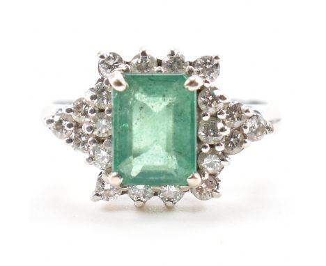 A 14ct white gold emerald and diamond cluster ring. The ring set with a central&nbsp; emerald cut emerald framed by round bri