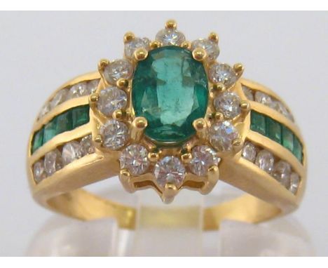 An emerald and diamond ring, the central oval cut emerald approx. 0.43 carat, in a surround of brilliants, to channel set eme