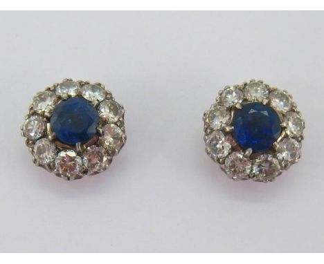 A pair of sapphire and diamond cluster ear studs, each central round cut sapphire 6.7-6.8mm diameter, in a surround of brilli