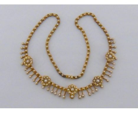 An Edwardian 15 carat gold and seed pearl necklace, the centre with five flower clusters above a shallow fringe, set througho