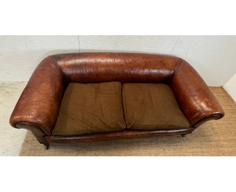 An antique leather two seater sofa on raised turned legs and castors (H86cm W190cm SH38cm)